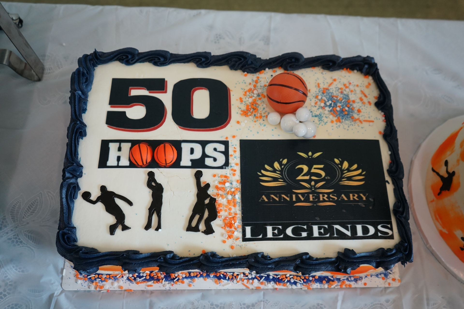 Cake celebrating 50 years of Hoops and a 25th anniversary. Silhouettes of basketball players, a basketball, and sprinkles.