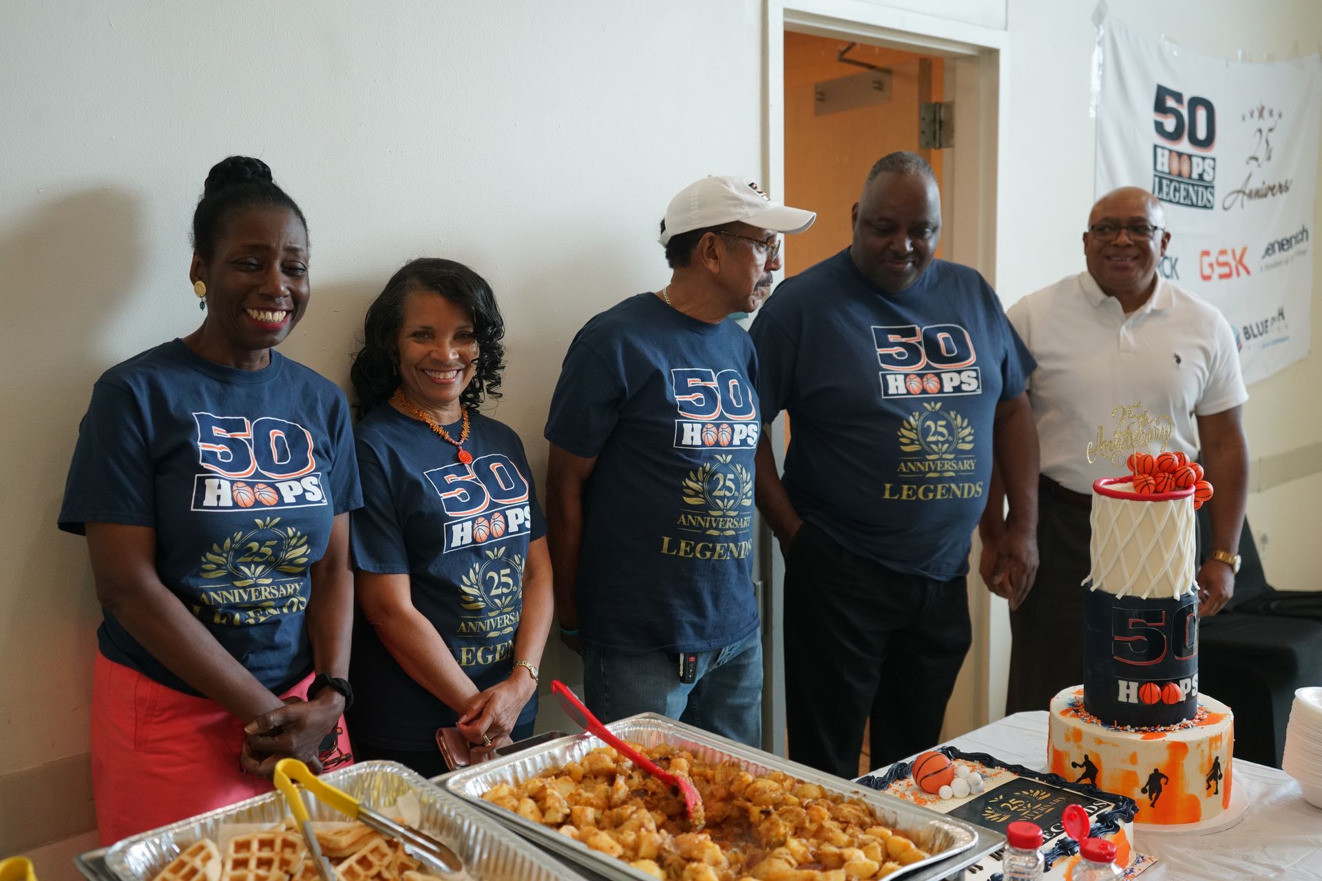 Group of people at a 50th-anniversary celebration, standing near a cake and food.
