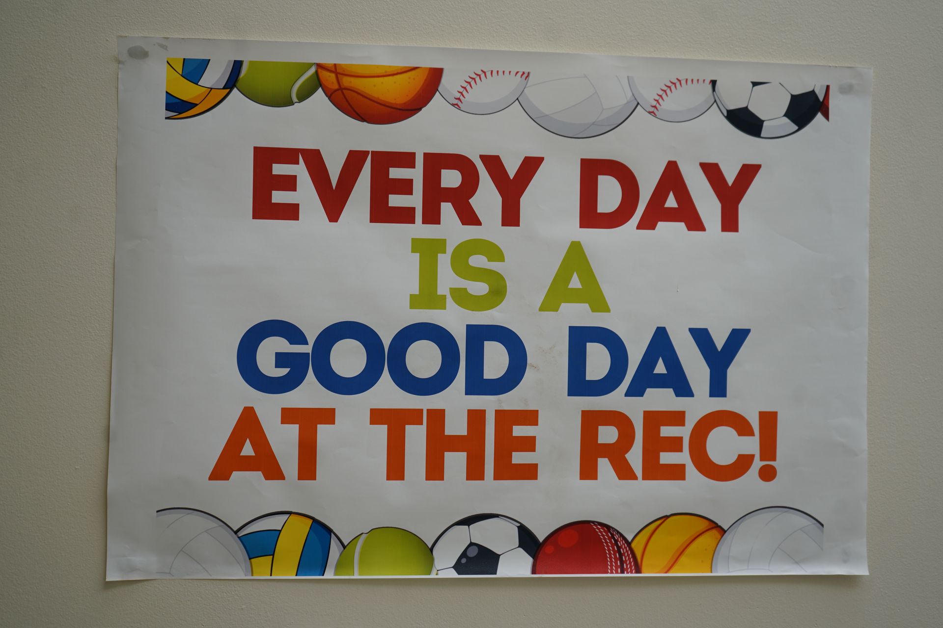 Sign with sports balls at top and bottom, text: 