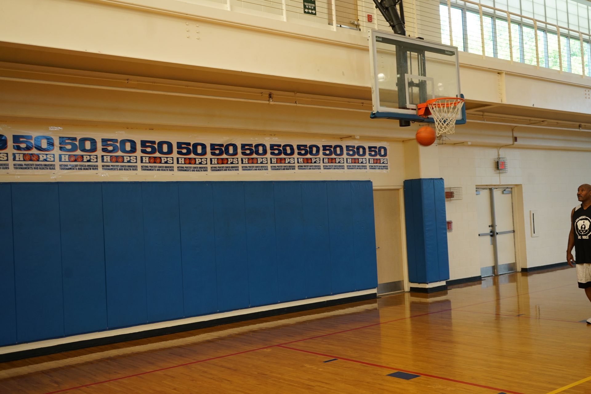 Basketball going through hoop in gym; person about to catch it.