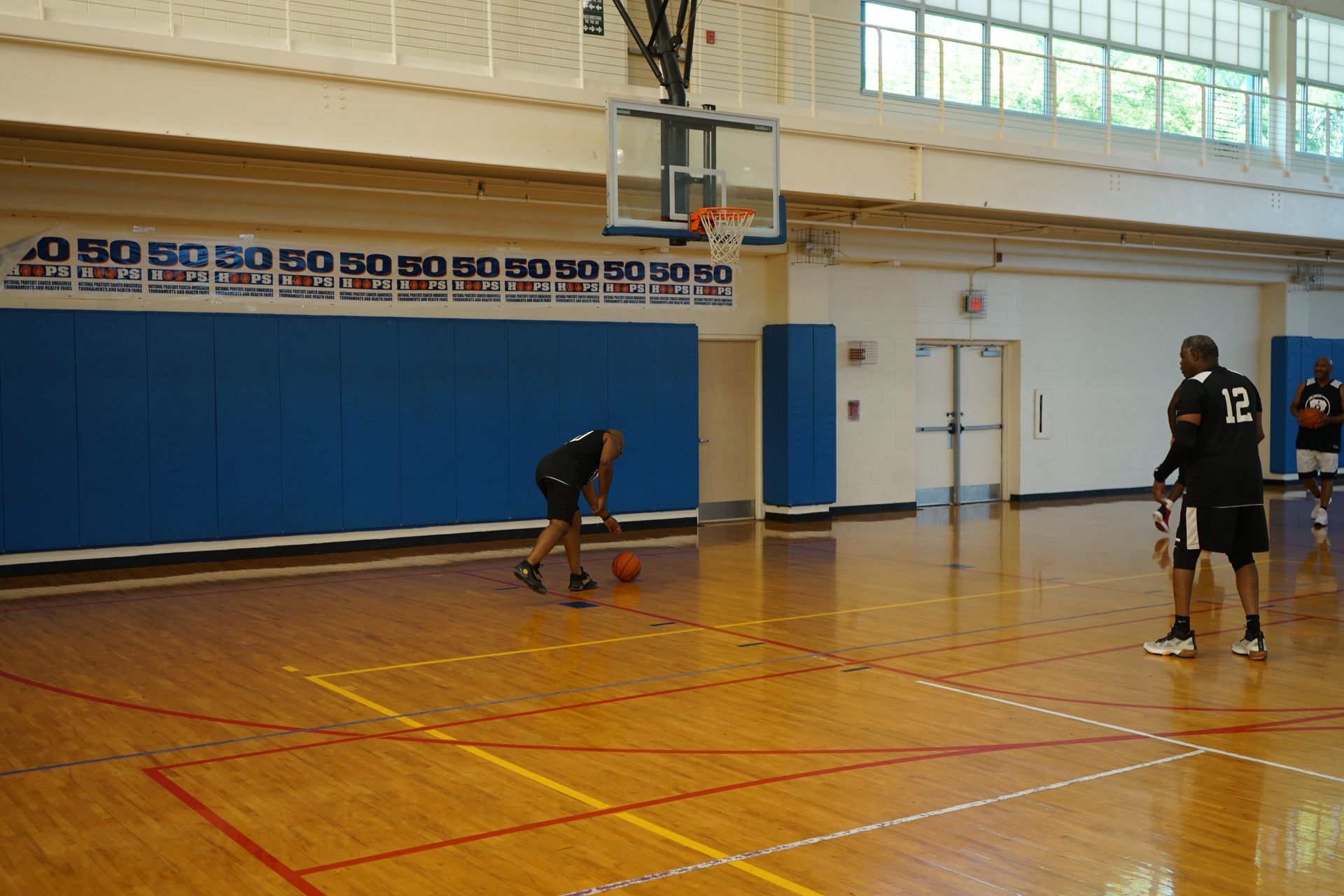 Basketball players on a wooden court. One dribbles, another stands with a ball near the hoop, indoors.