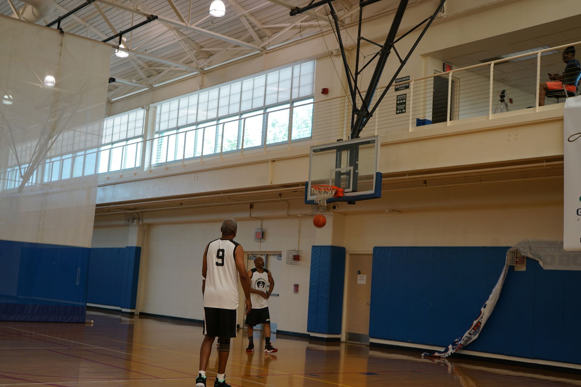 Basketball players on a court, one shooting toward the hoop, ball mid-air.