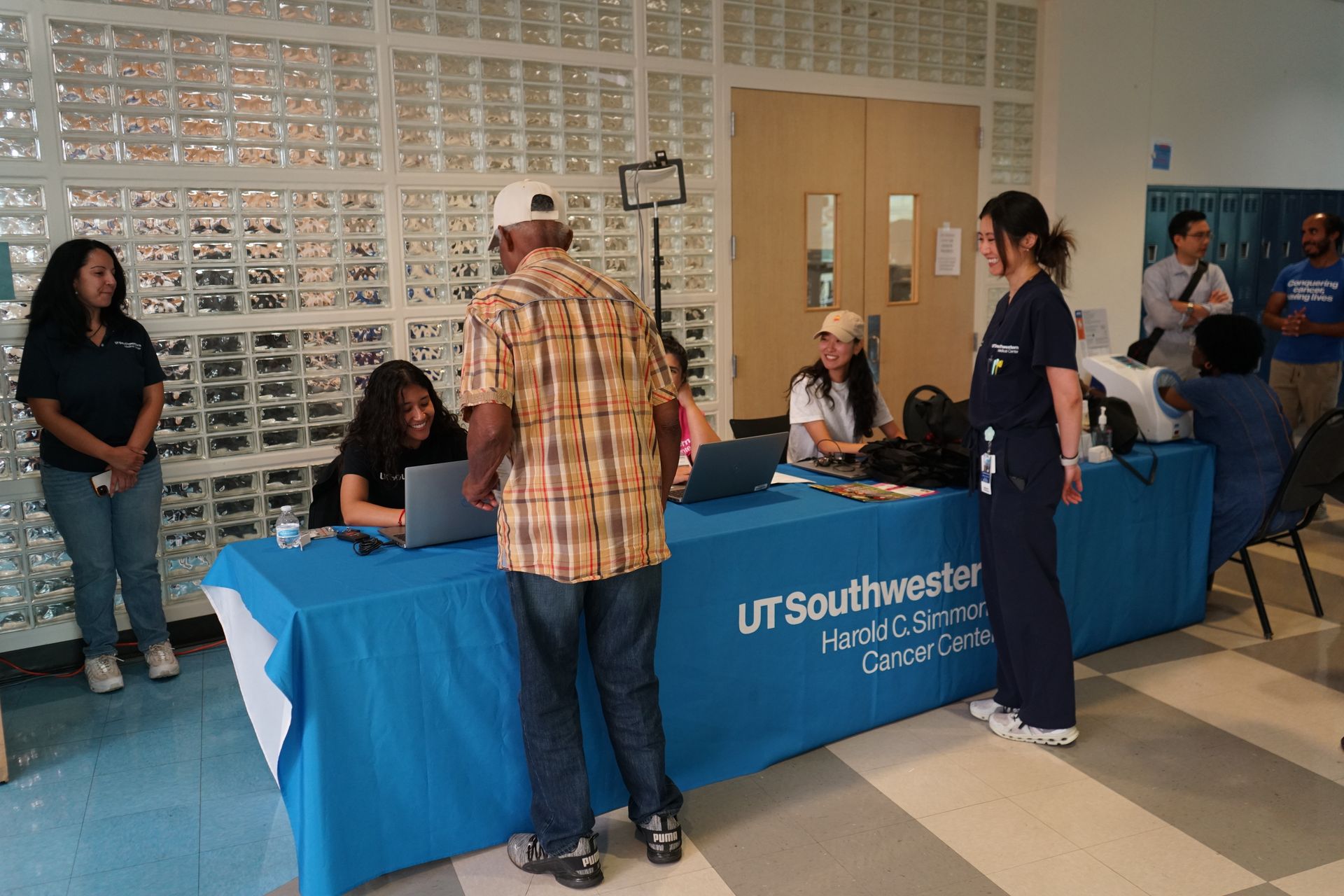 People at a health services table, with signage for UT Southwestern. Blue table cover, bright setting.