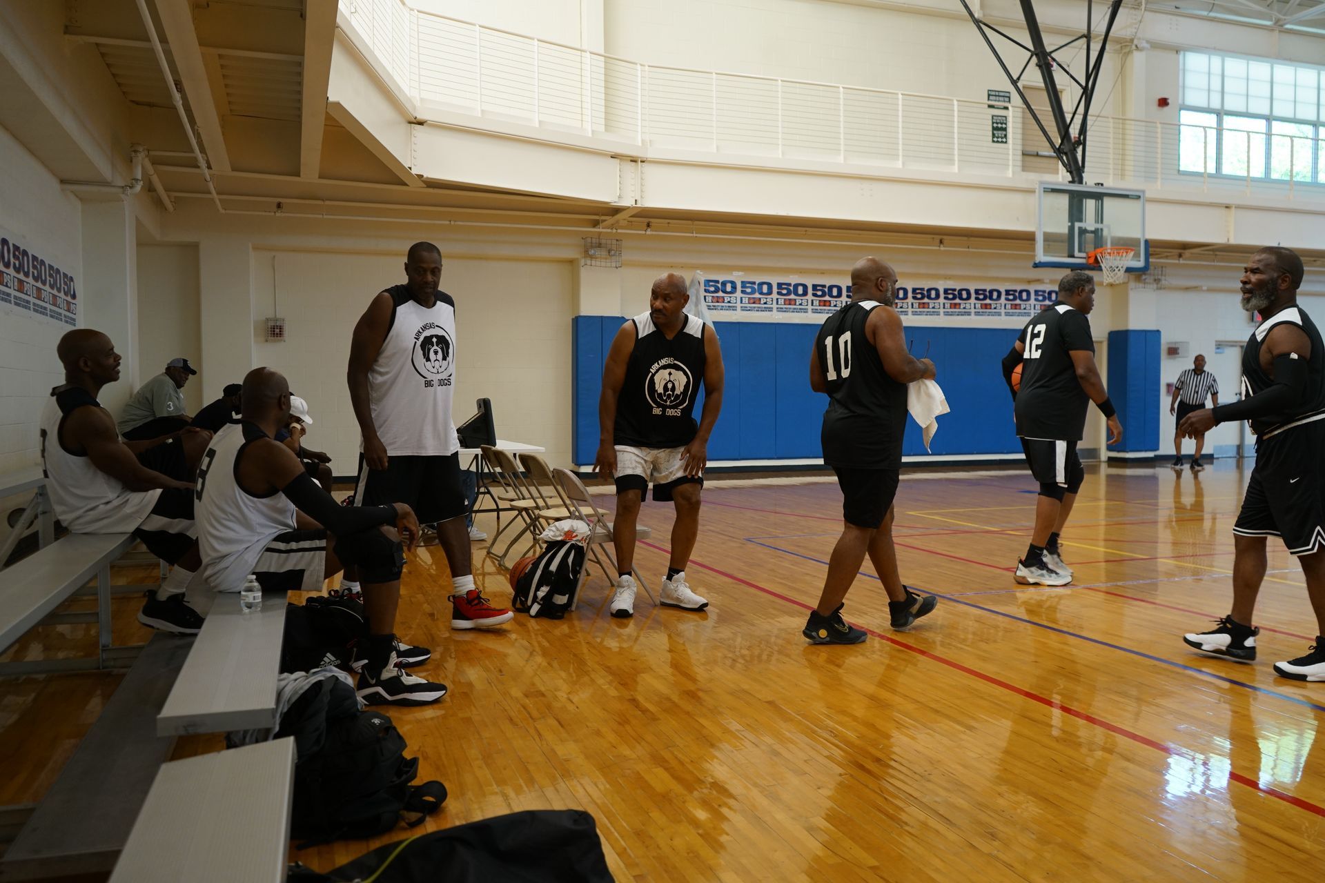Basketball players in a gym, some in uniform, others on the bench, preparing to play.