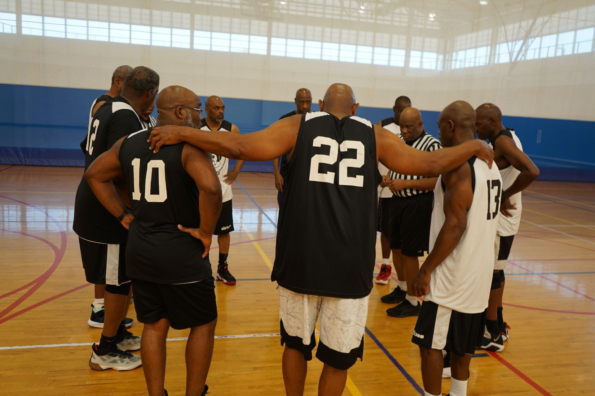 Basketball players huddle on court, arms around each other, wearing black and white jerseys.