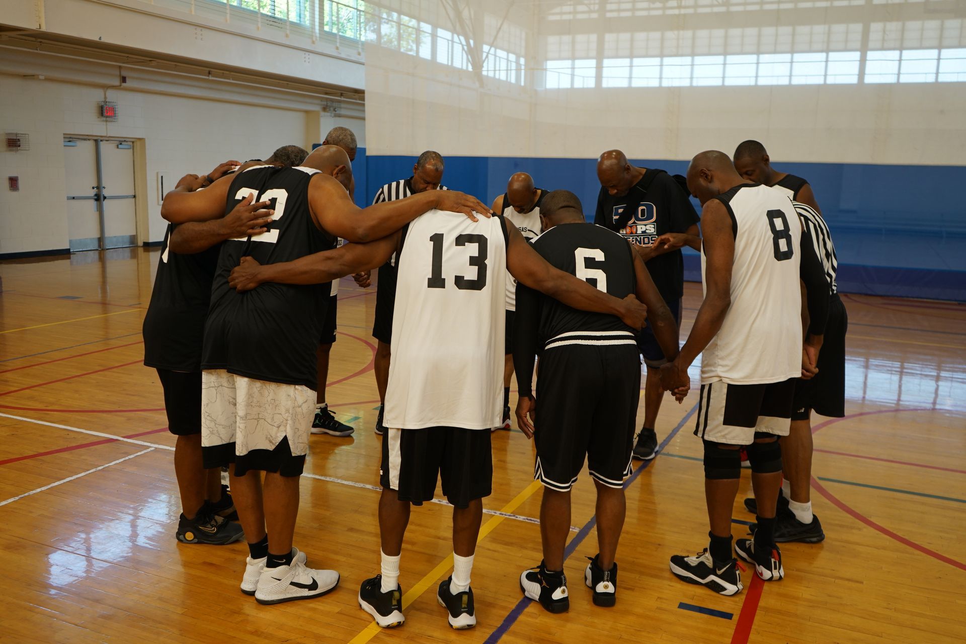 Basketball players in a huddle on a court. All wearing black and white jerseys, arms around each other.