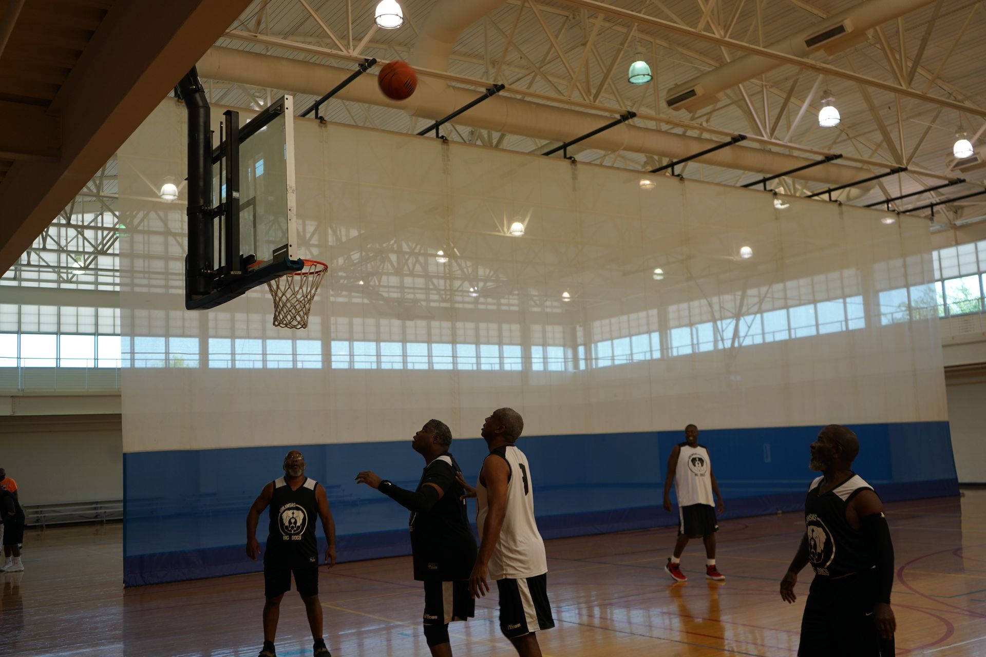 Basketball game in a gym: ball in air near hoop, players in action.