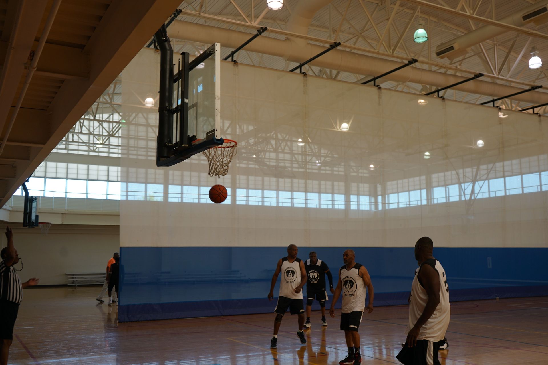 Basketball going through a hoop in a gym. Players watch, blue and white wall.