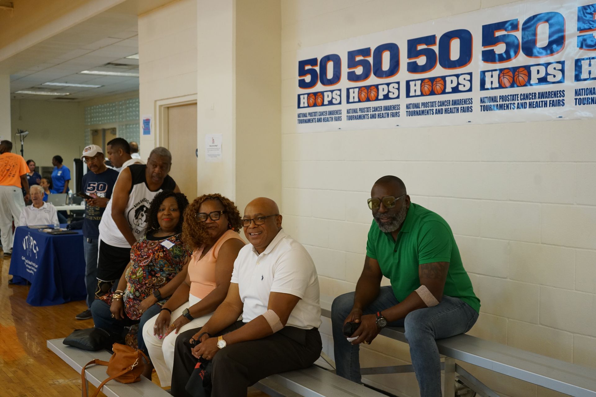 People seated on a bench, watching a basketball event with a 