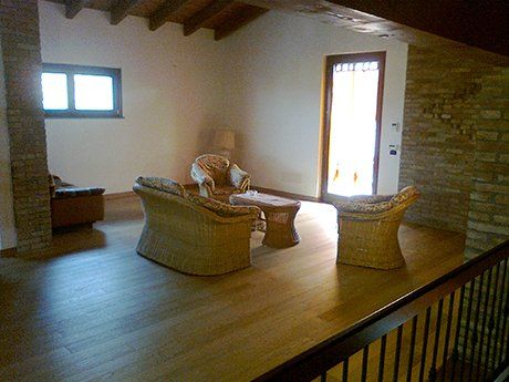 vista angolare di una stanza con poltrone, divano, parete in pietra e soffitto in legno