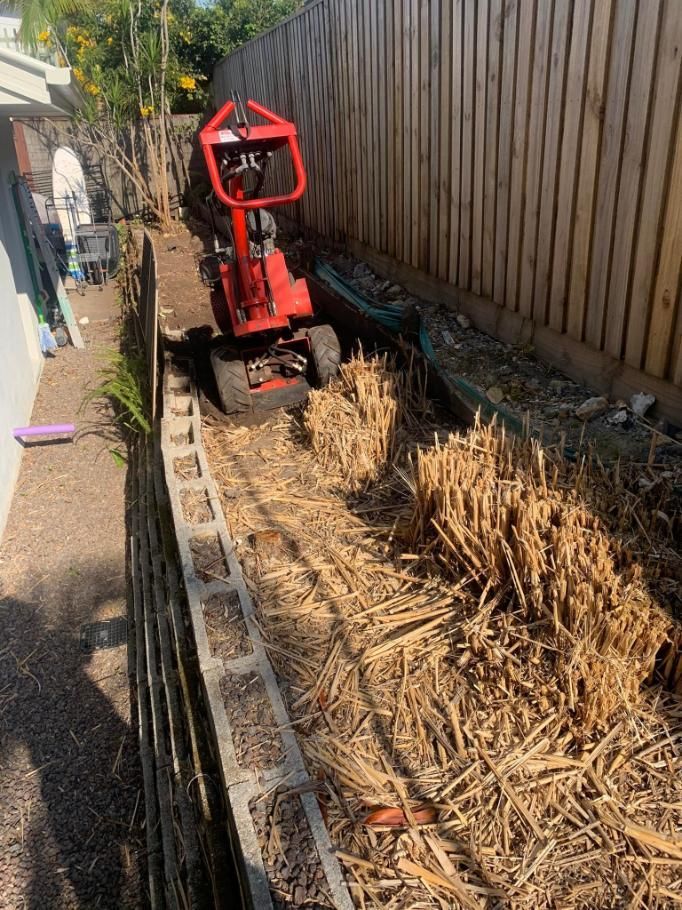A Red Tractor Is Driving Down A Dirt Road Next To A Wooden Fence — Noosa Tree Stump Removal In Sunrise Beach, QLD