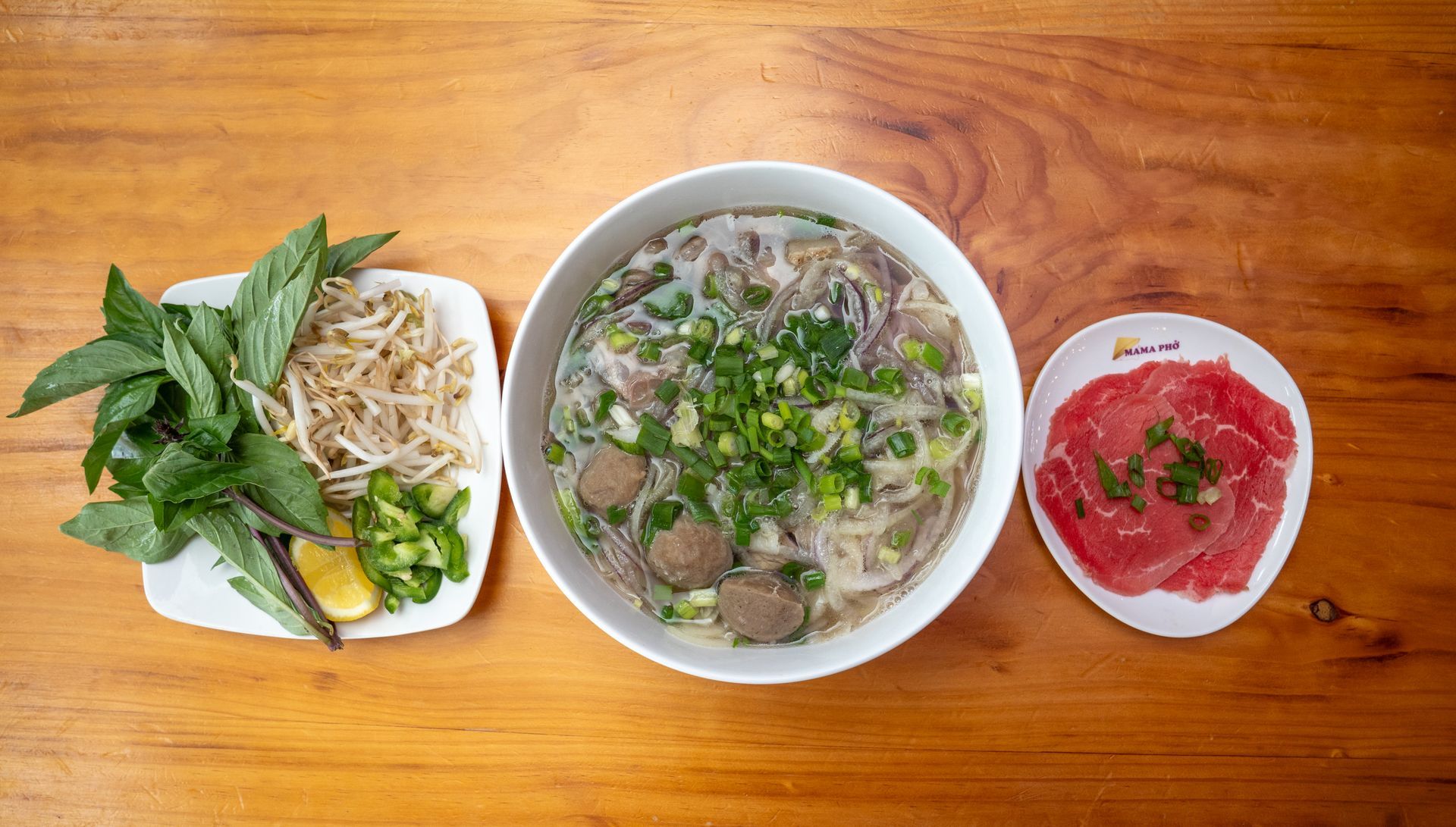 A bowl of soup and a plate of meat are on a wooden table.