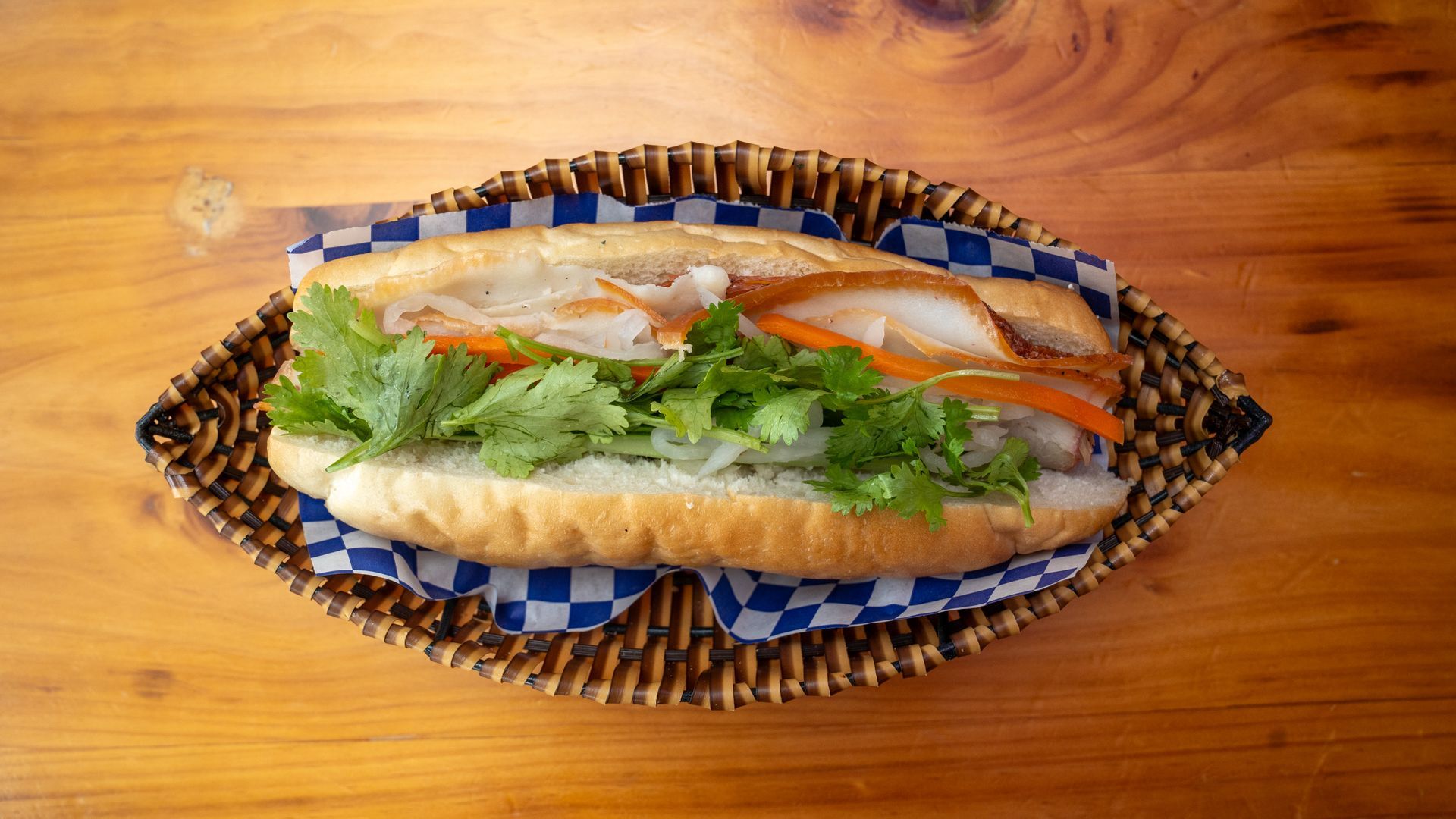 A sandwich is sitting in a basket on a wooden table.