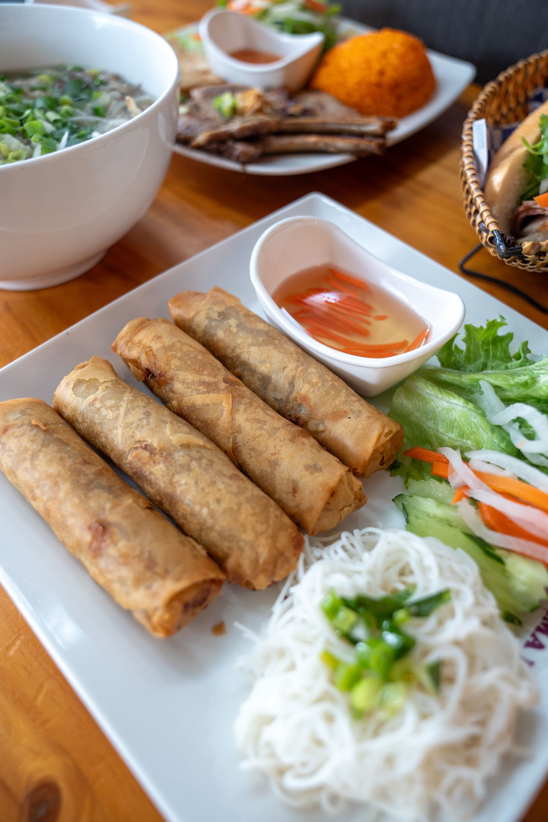 A plate of spring rolls with noodles and vegetables on a wooden table.
