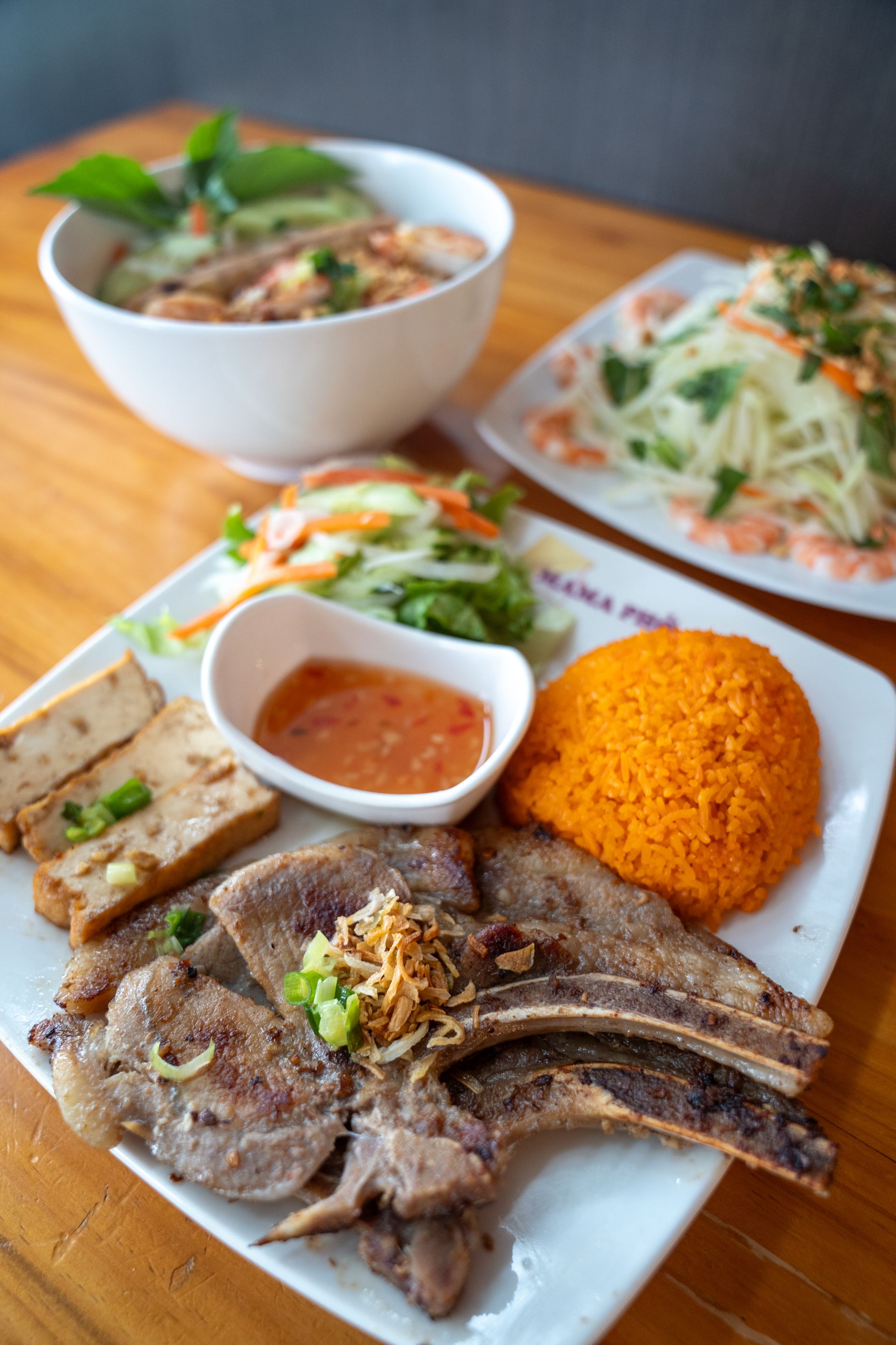 A plate of food with meat , rice and a bowl of soup on a wooden table.