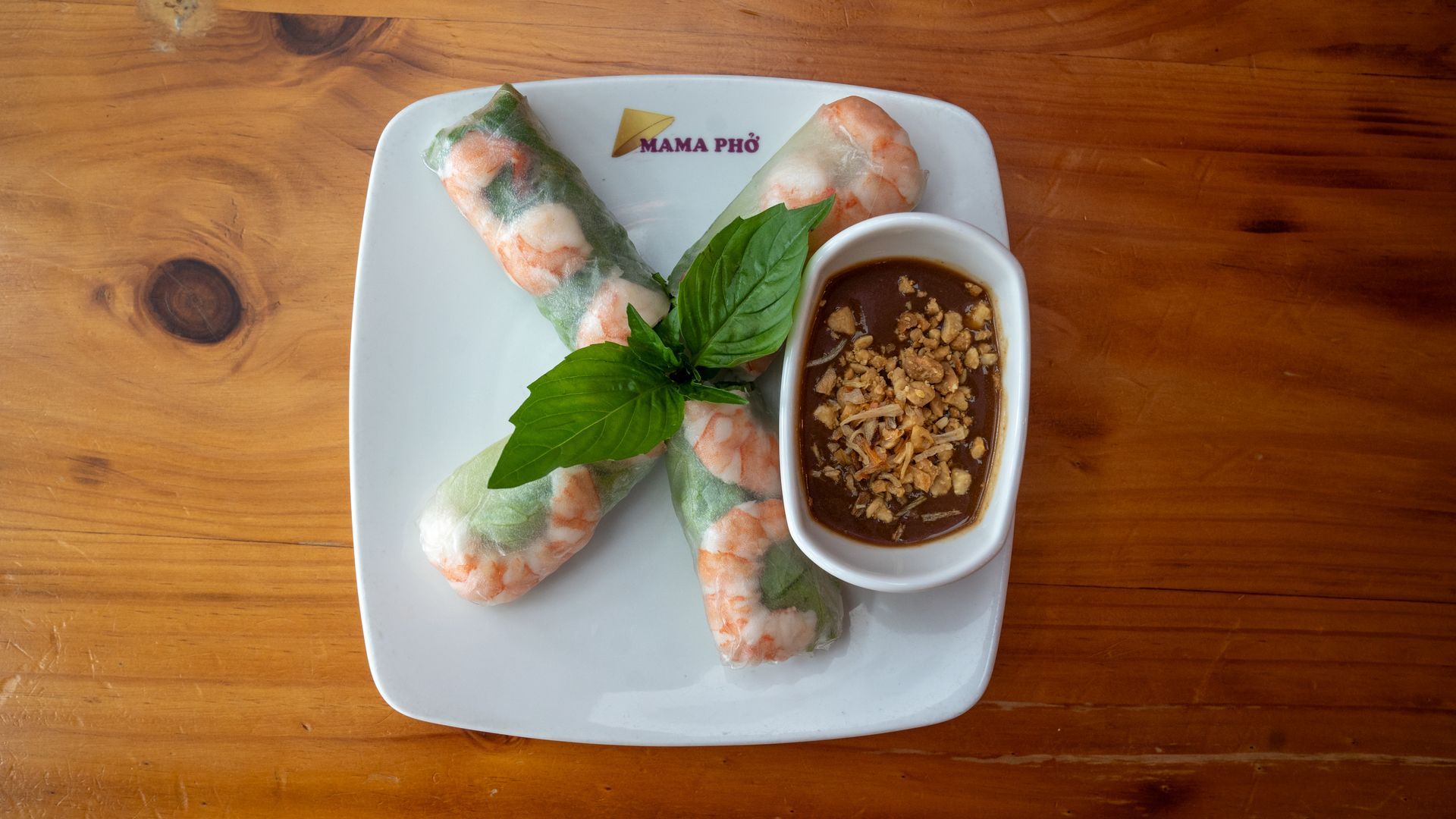 A white plate topped with shrimp rolls and a bowl of dipping sauce on a wooden table.