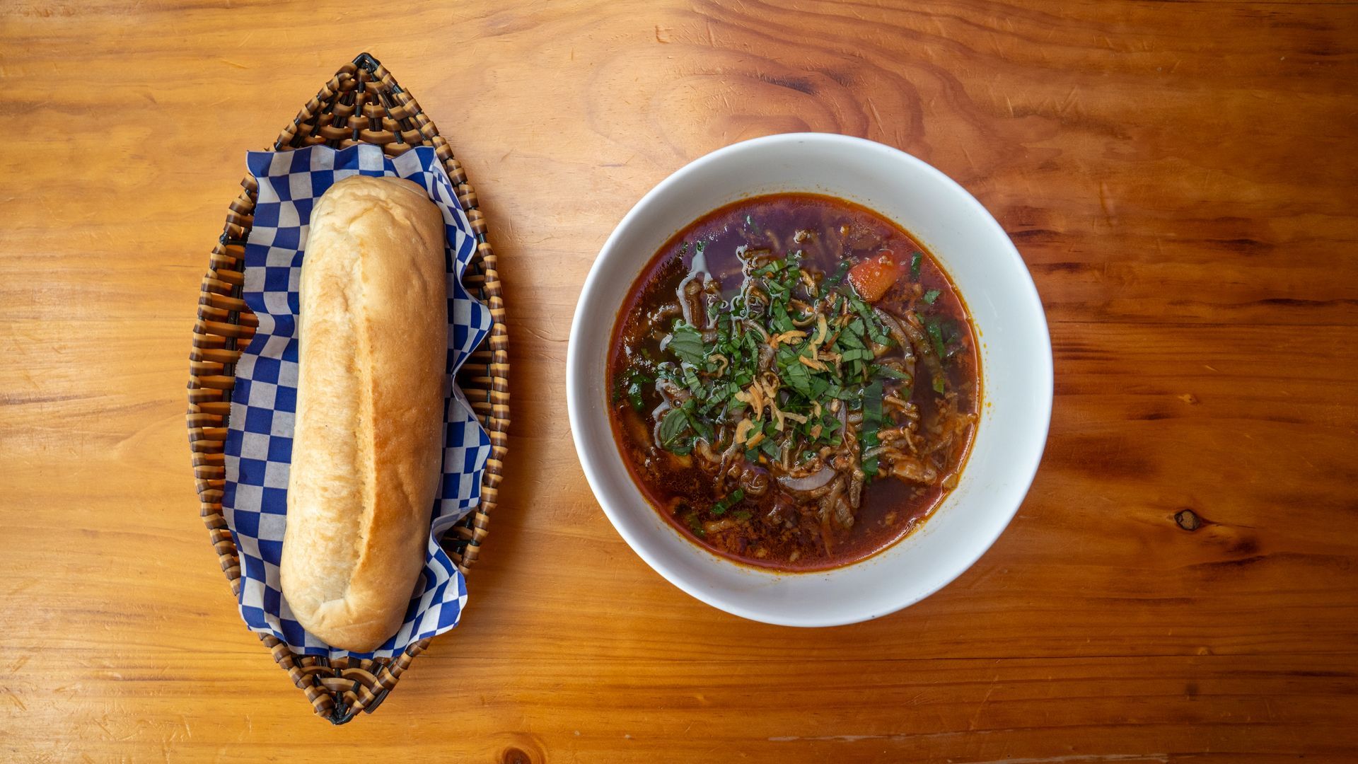 A bowl of soup and a loaf of bread on a wooden table.