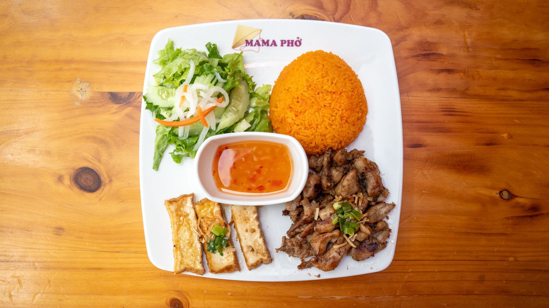 A plate of food with rice , meat , and vegetables on a wooden table.
