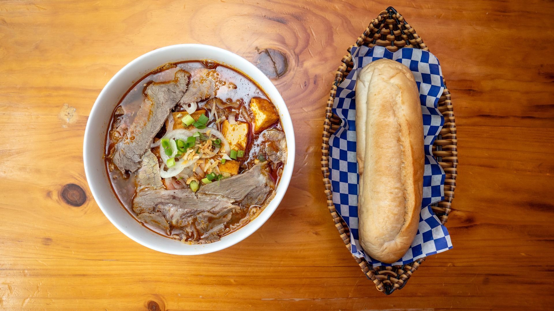 A bowl of soup and a loaf of bread on a wooden table.