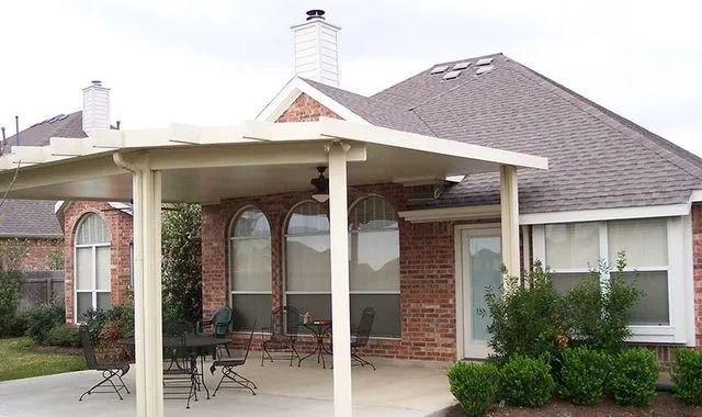 A patio with a table and chairs under a covered patio in front of a brick house.