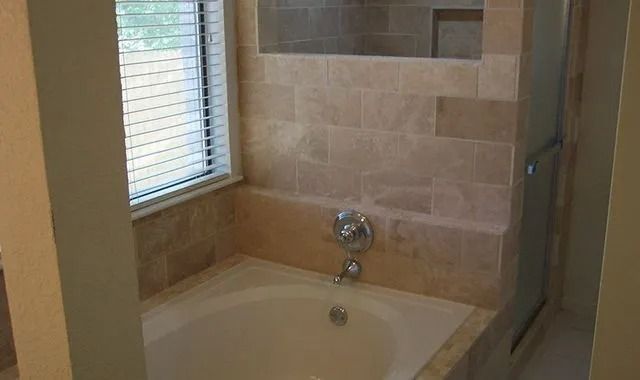 A bathroom with a tub , shower and window.