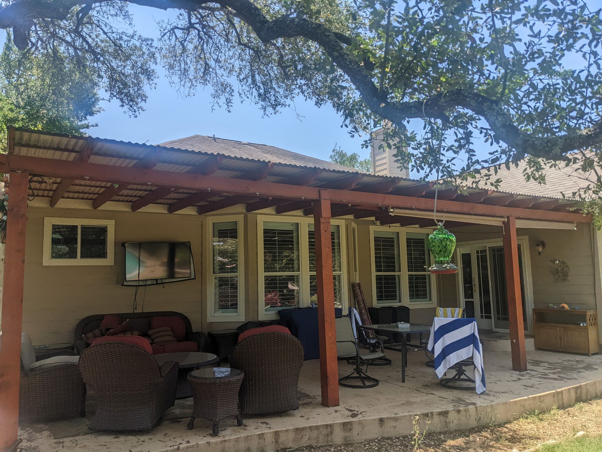 A patio with a pergola and a couch , chairs , tables and a television.