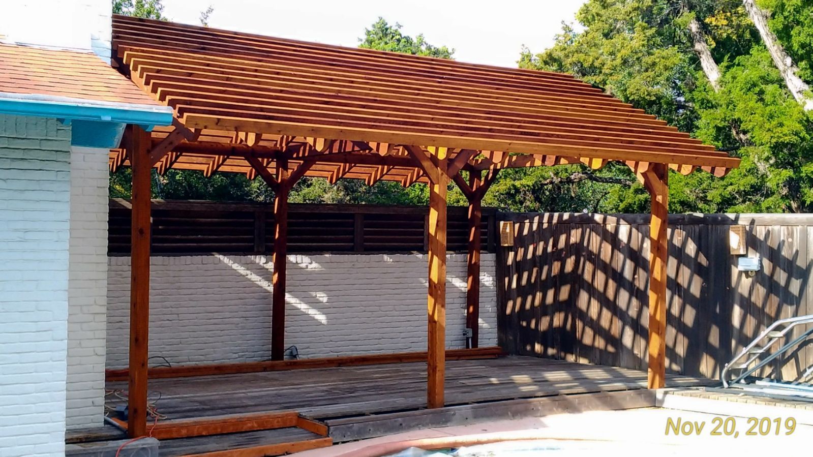 A wooden pergola is being built in front of a white brick building.