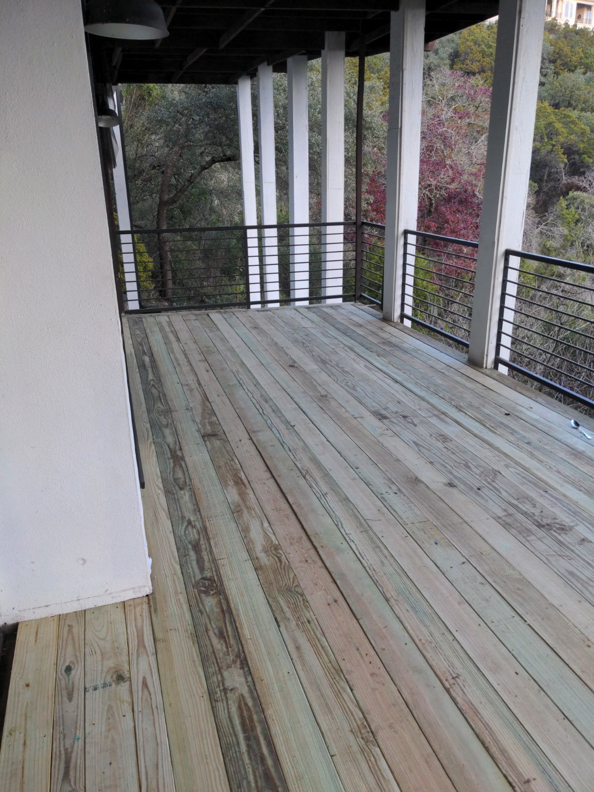 A large wooden deck with a railing and trees in the background.