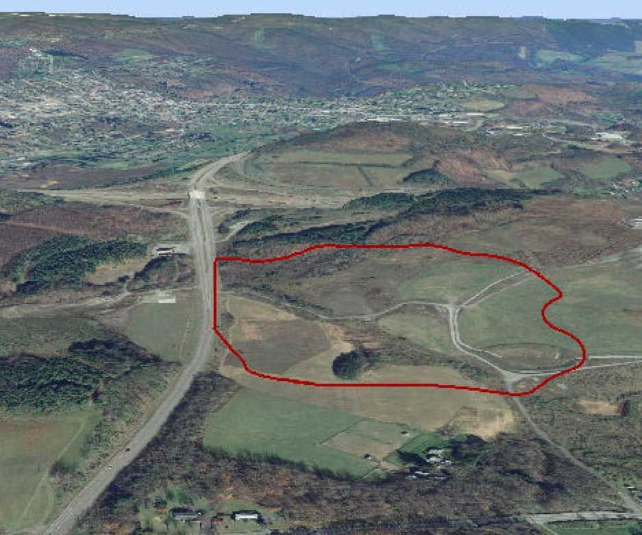 Aerial view of land outlined in red, likely a development site, next to a highway and town. Autumn colors dominate the landscape.