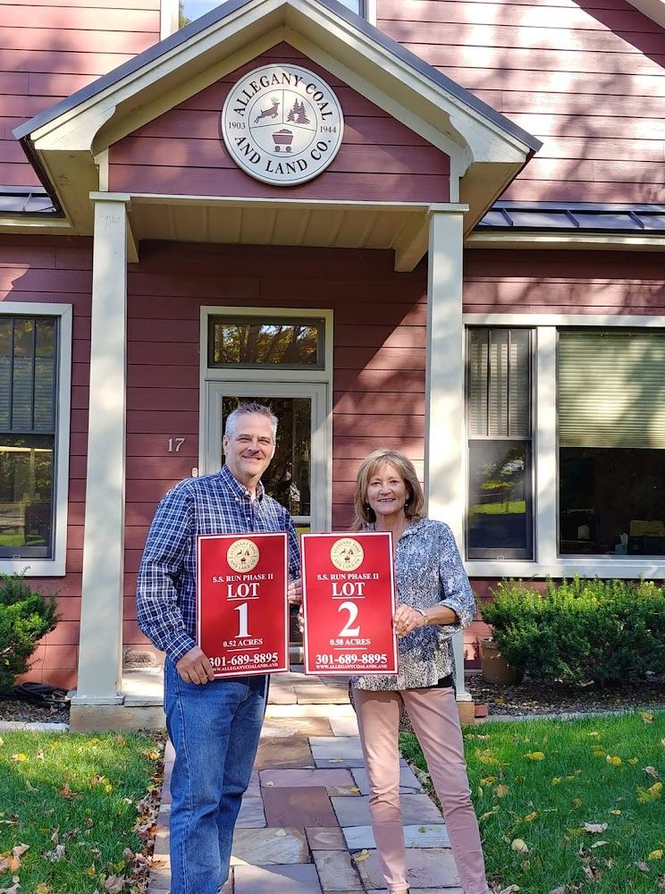 A man and a woman are holding signs in front of a red house.
