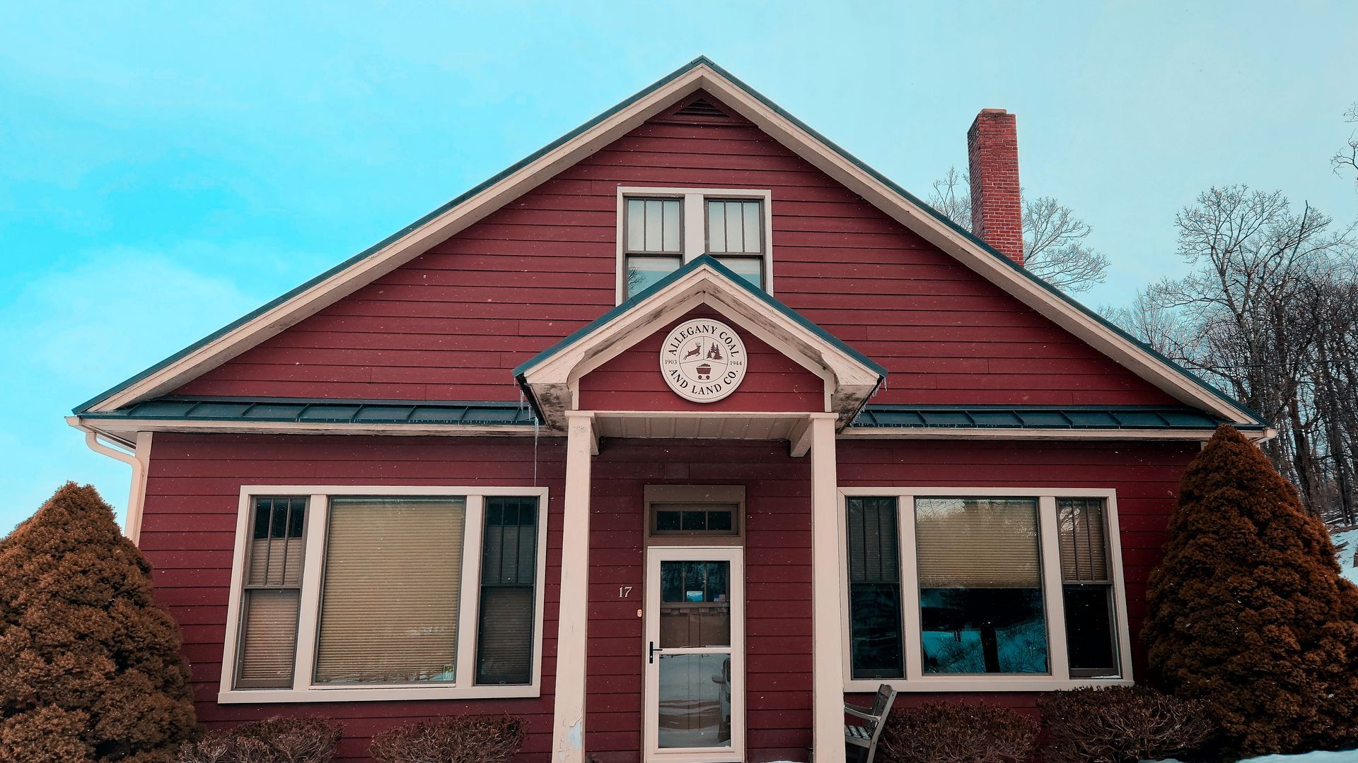 Red two-story house with a gable roof, white trim, and a front porch; set against a bright blue sky.