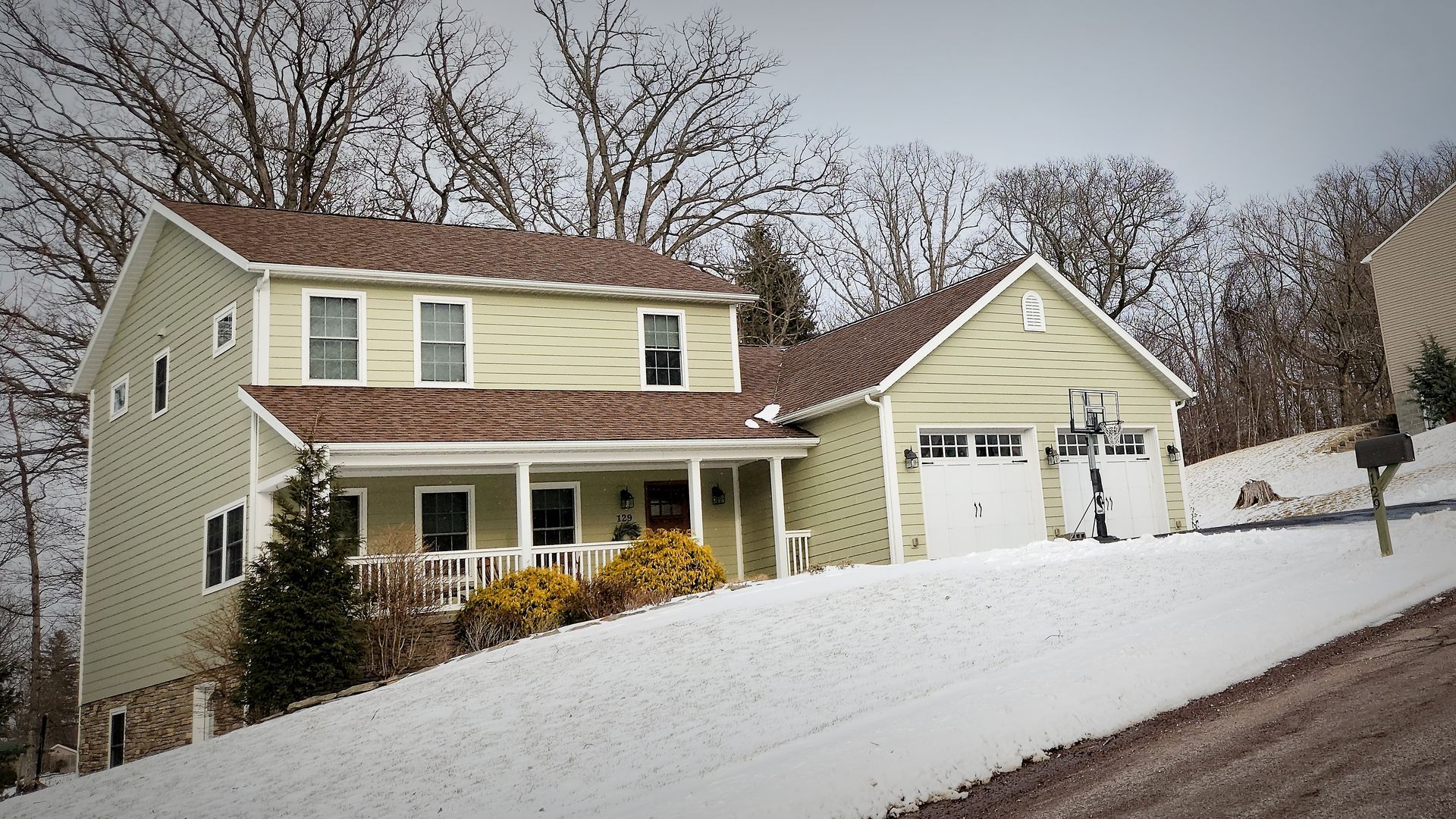Two-story house with a green exterior, brown roof, and attached garage, set on a snowy hill.