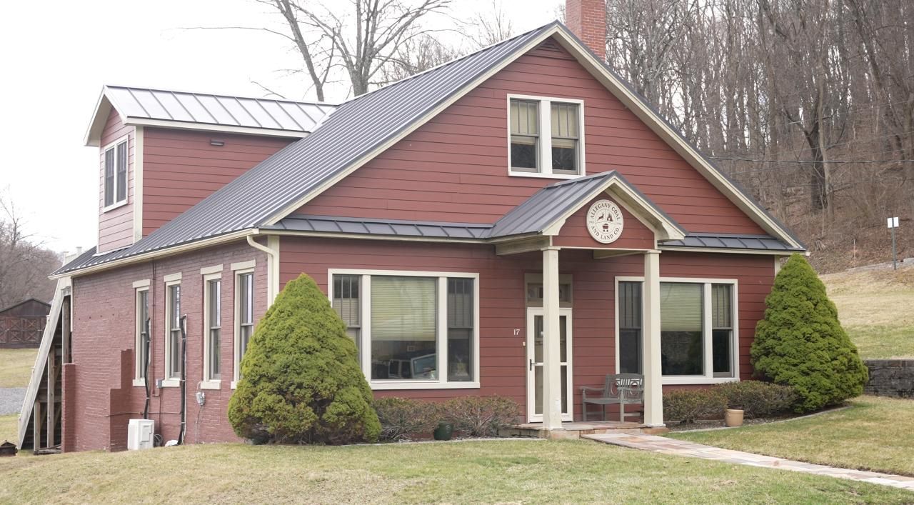 Red brick house with a dark roof, white trim, and small front yard, in front of a hillside with bare trees.