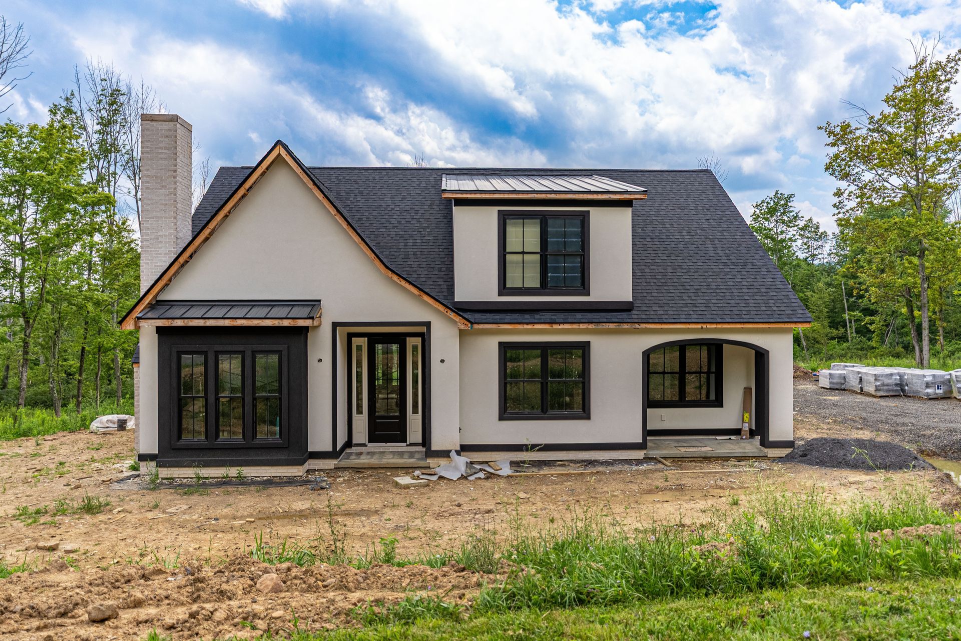 Beige house with black trim, a chimney, and dark roof; under construction in a grassy area.