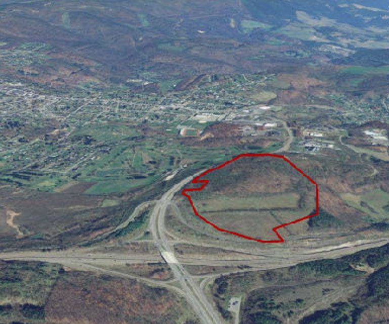 Aerial view of a hilly landscape with a red outline marking a plot of land, near a highway and town.