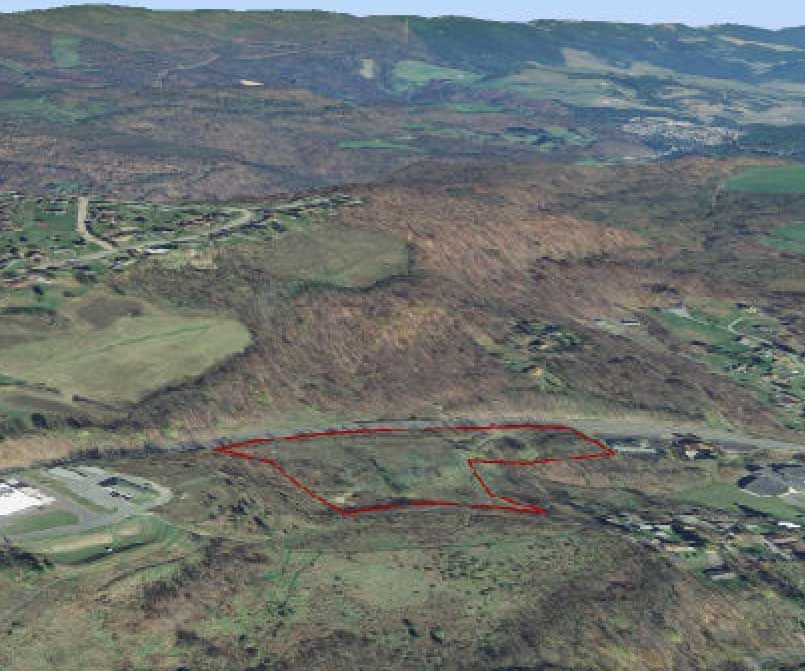 Aerial view of a hilly landscape with a red outline marking a plot of land. Buildings and roads are visible in the distance.