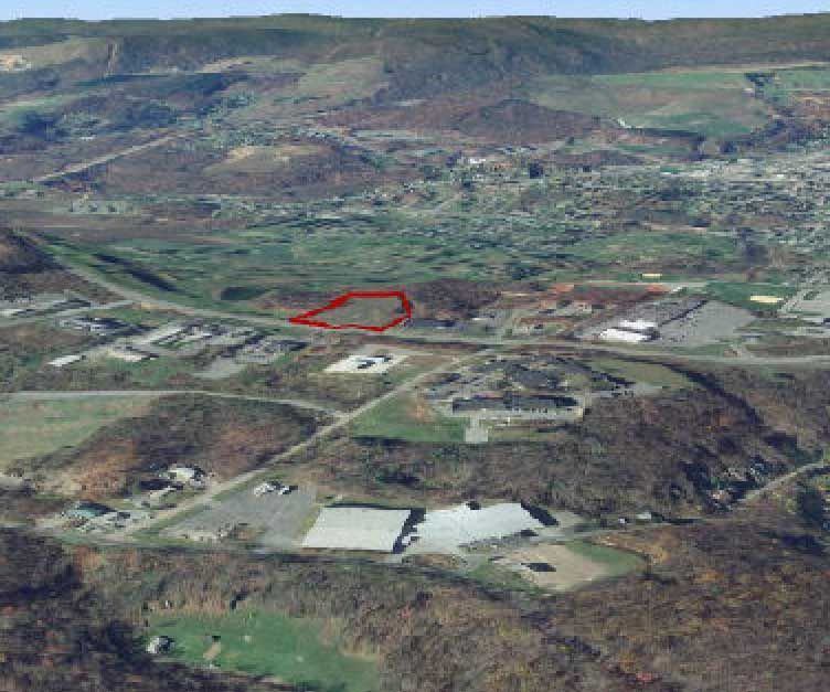 Aerial view of a landscape with a red polygon highlighting a plot of land, with buildings and roads in the foreground and hills in the background.