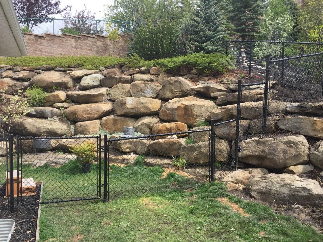 A backyard with a chain link fence and a large rock wall.