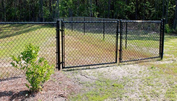 A chain link fence with a gate in the middle of a grassy field.