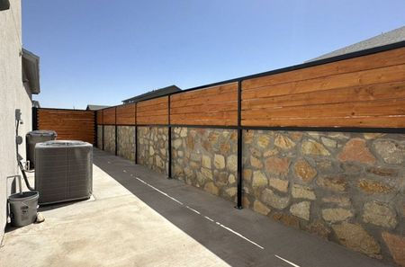 A beautiful stone wall with wood and metal fence along a concrete slab.