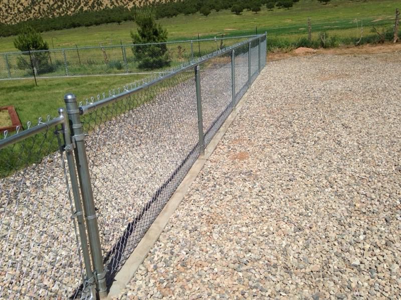 A chain link fence is surrounding a gravel driveway.