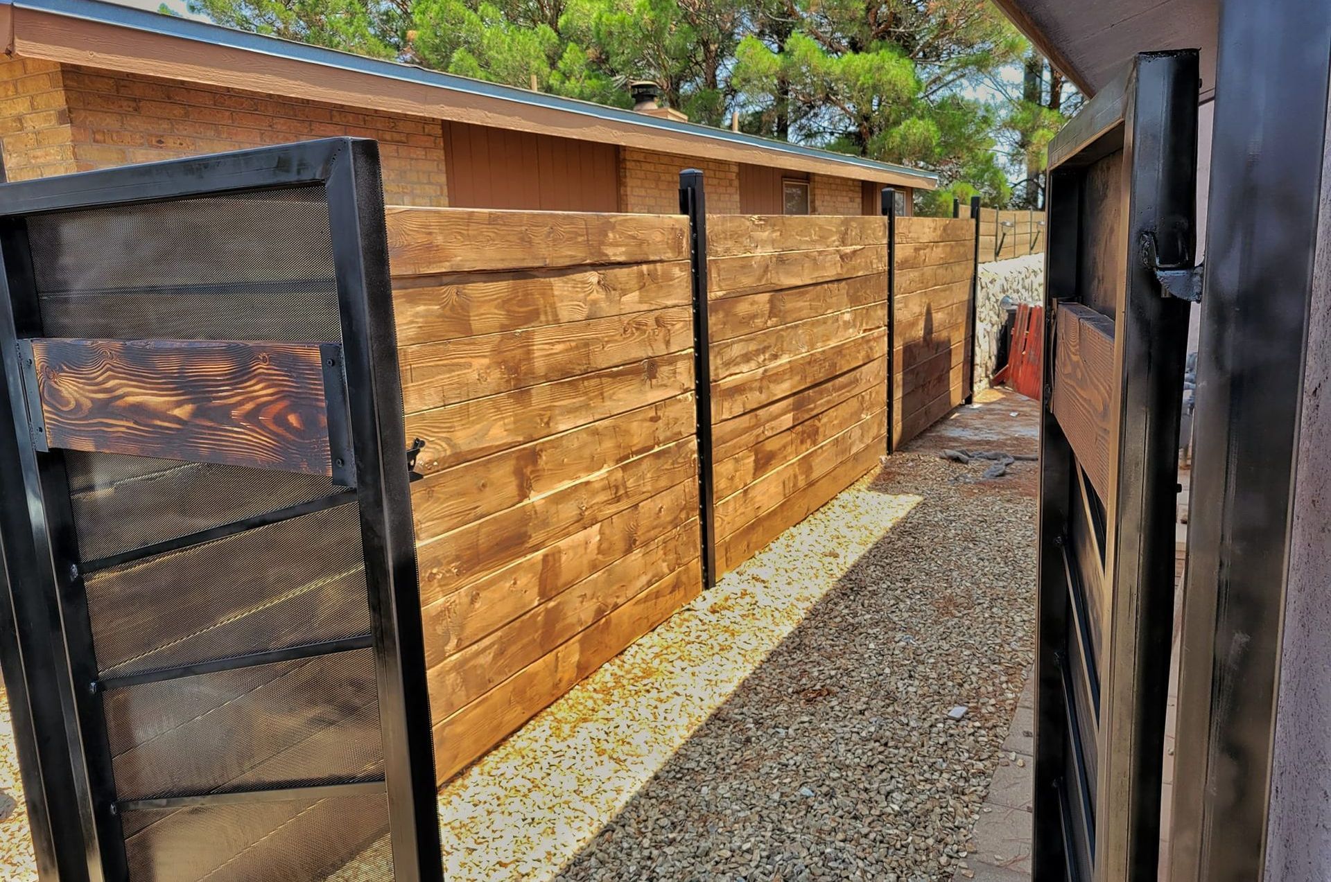 A wooden fence lines a gravel pathway in a side yard