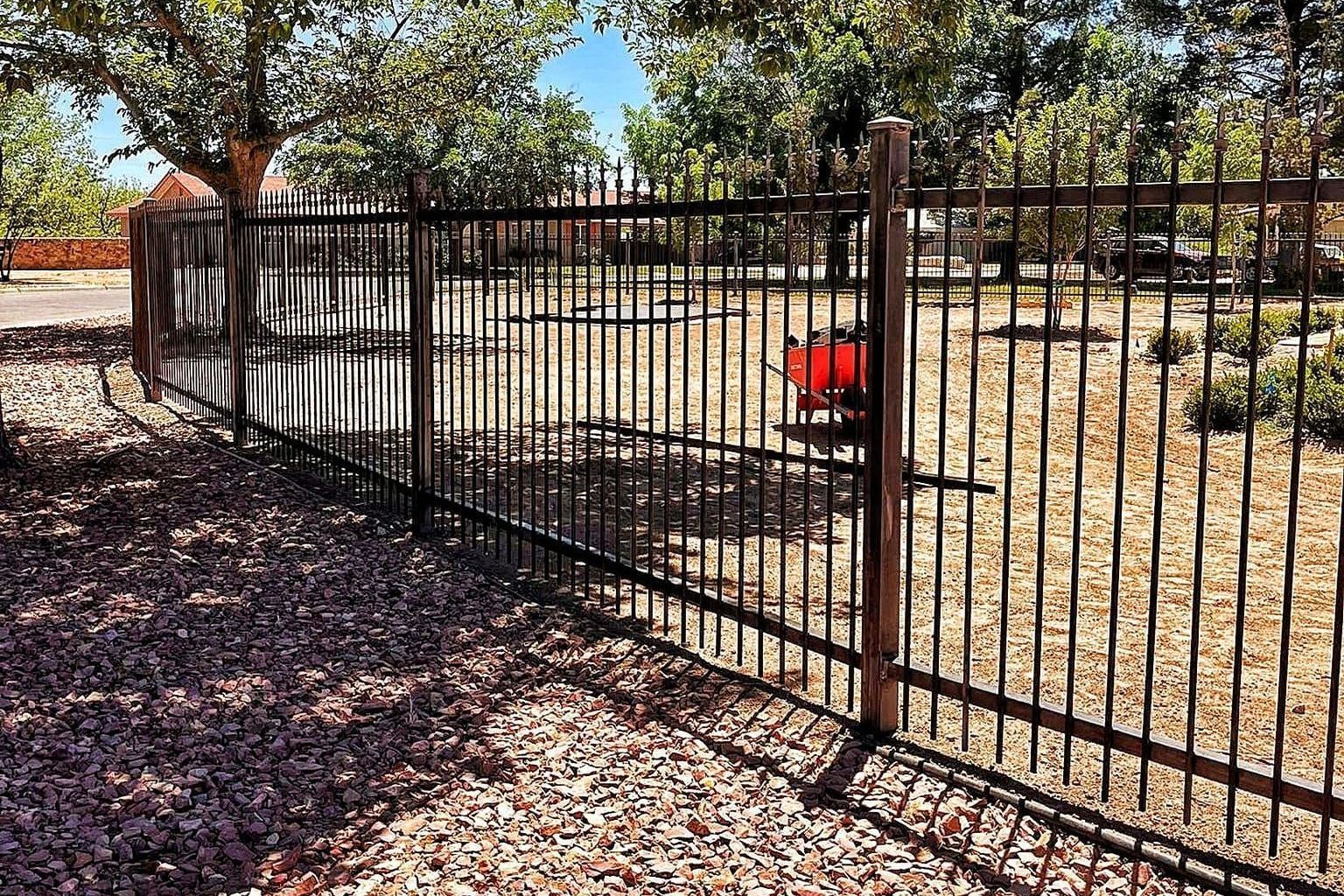 Wrought iron fence separating a gravel and grass yard