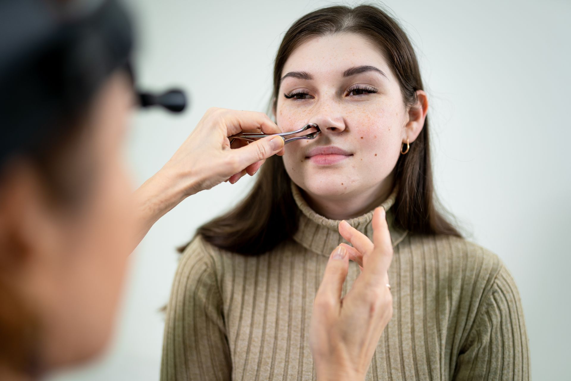 A woman with Deviated Septum is getting her nose examined by a doctor.