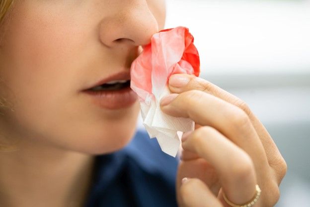 A woman using a tissue to stop a nosebleed 