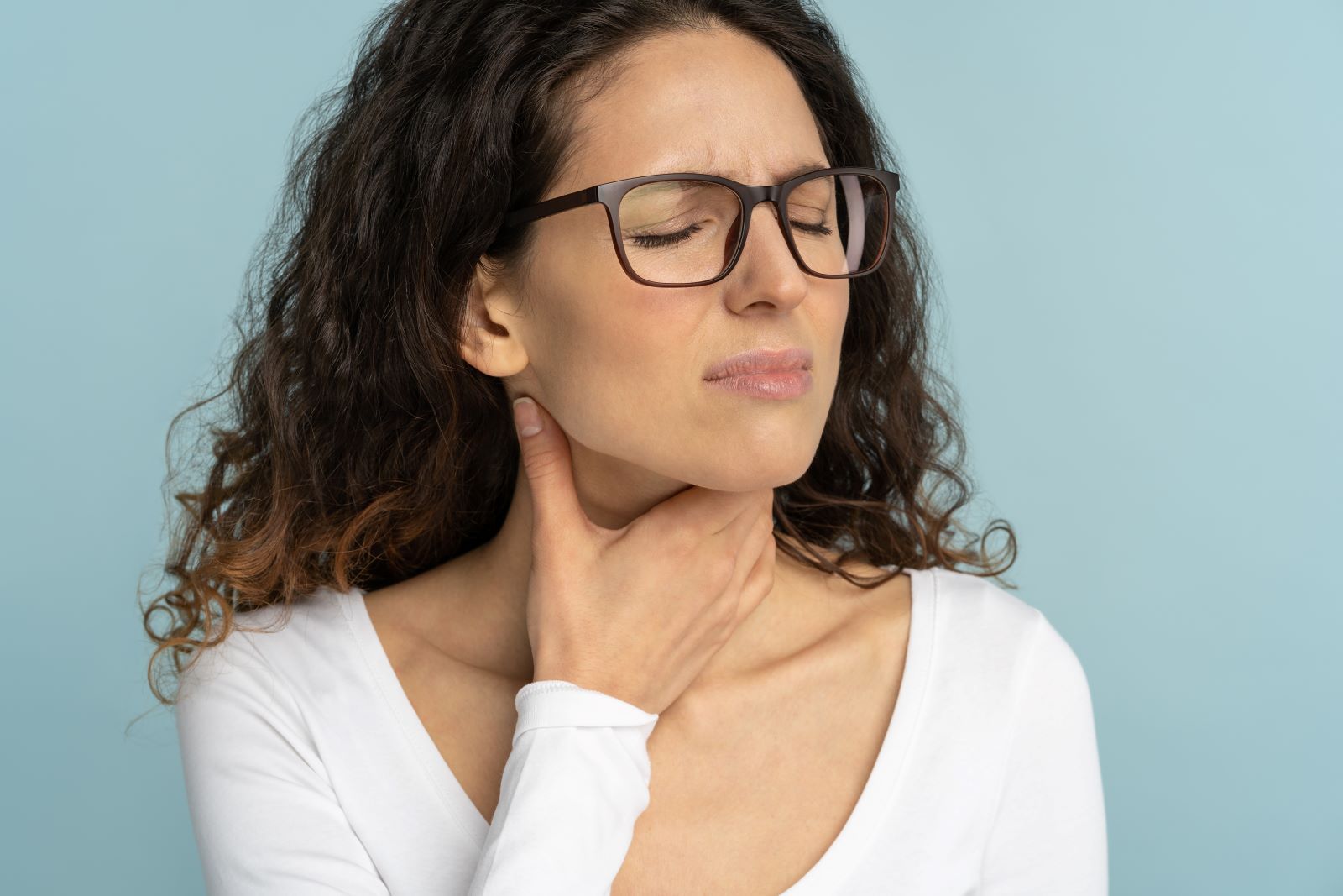 a woman wearing glasses is holding her neck in pain from a tonsil stone