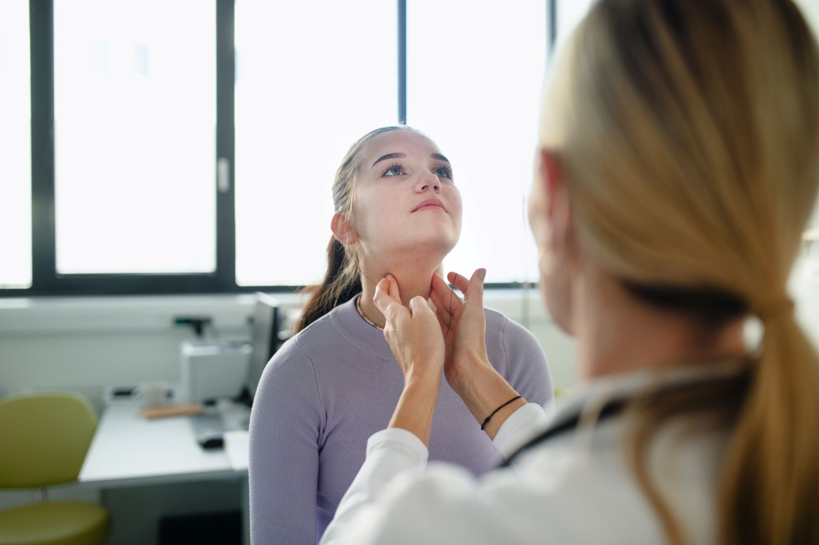 Doctor examining a patient's neck in a medical office.