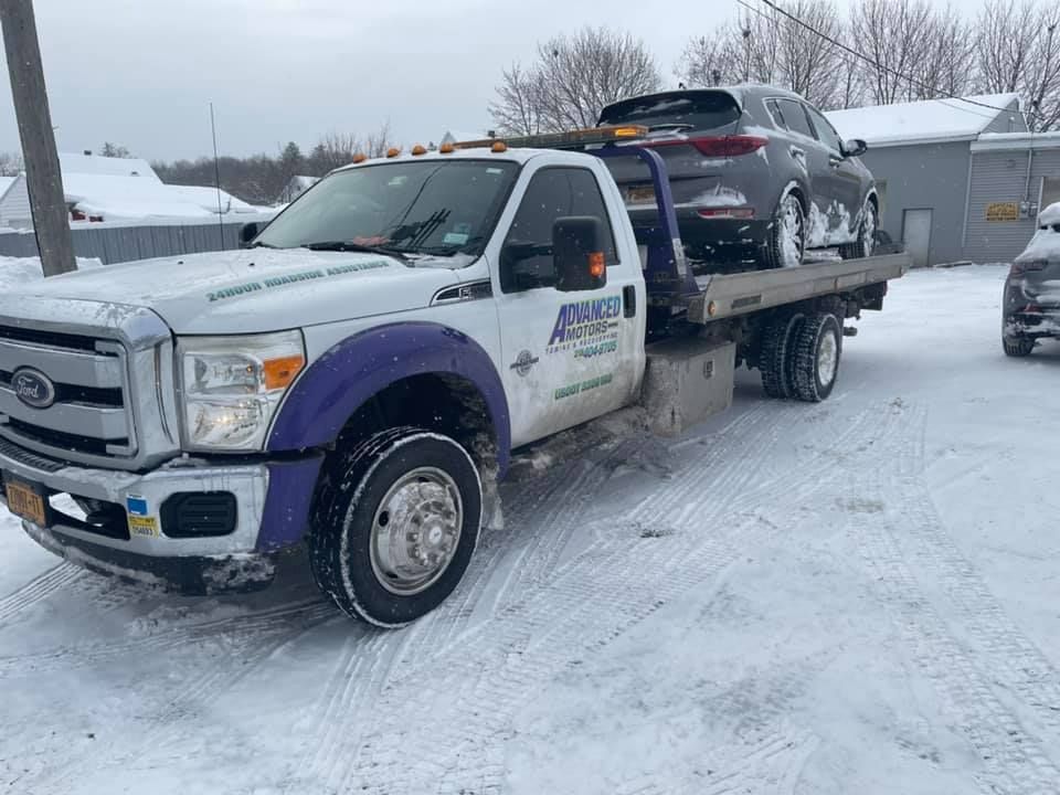 A tow truck is towing a car in the snow.