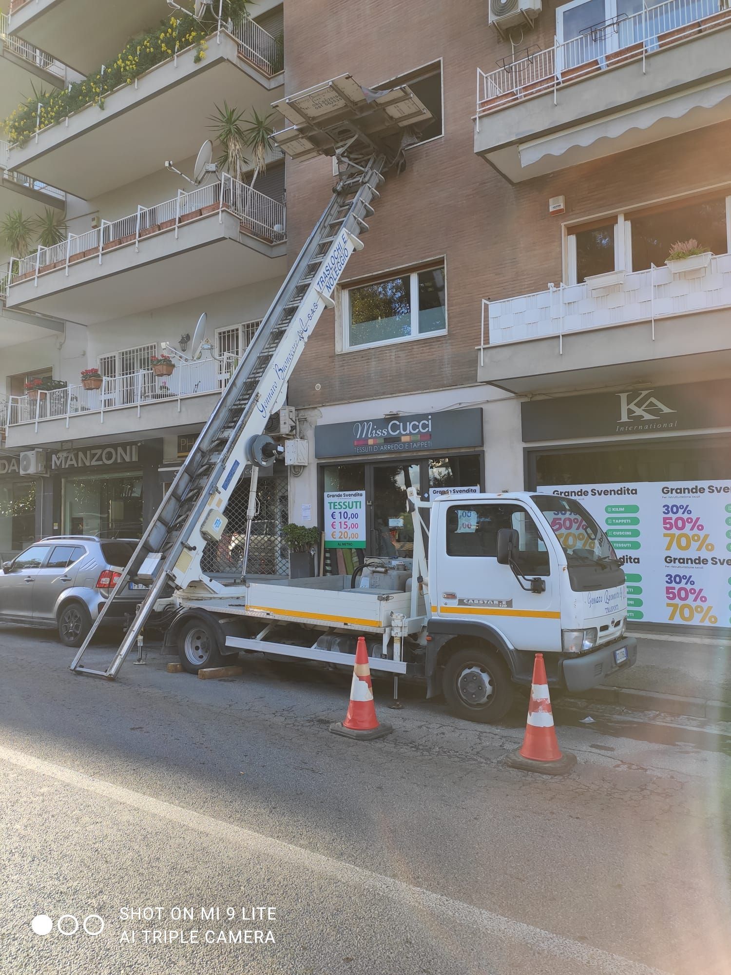 Un camion con un elevatore esteso scarica oggetti dalla finestra di un appartamento in una strada cittadina.