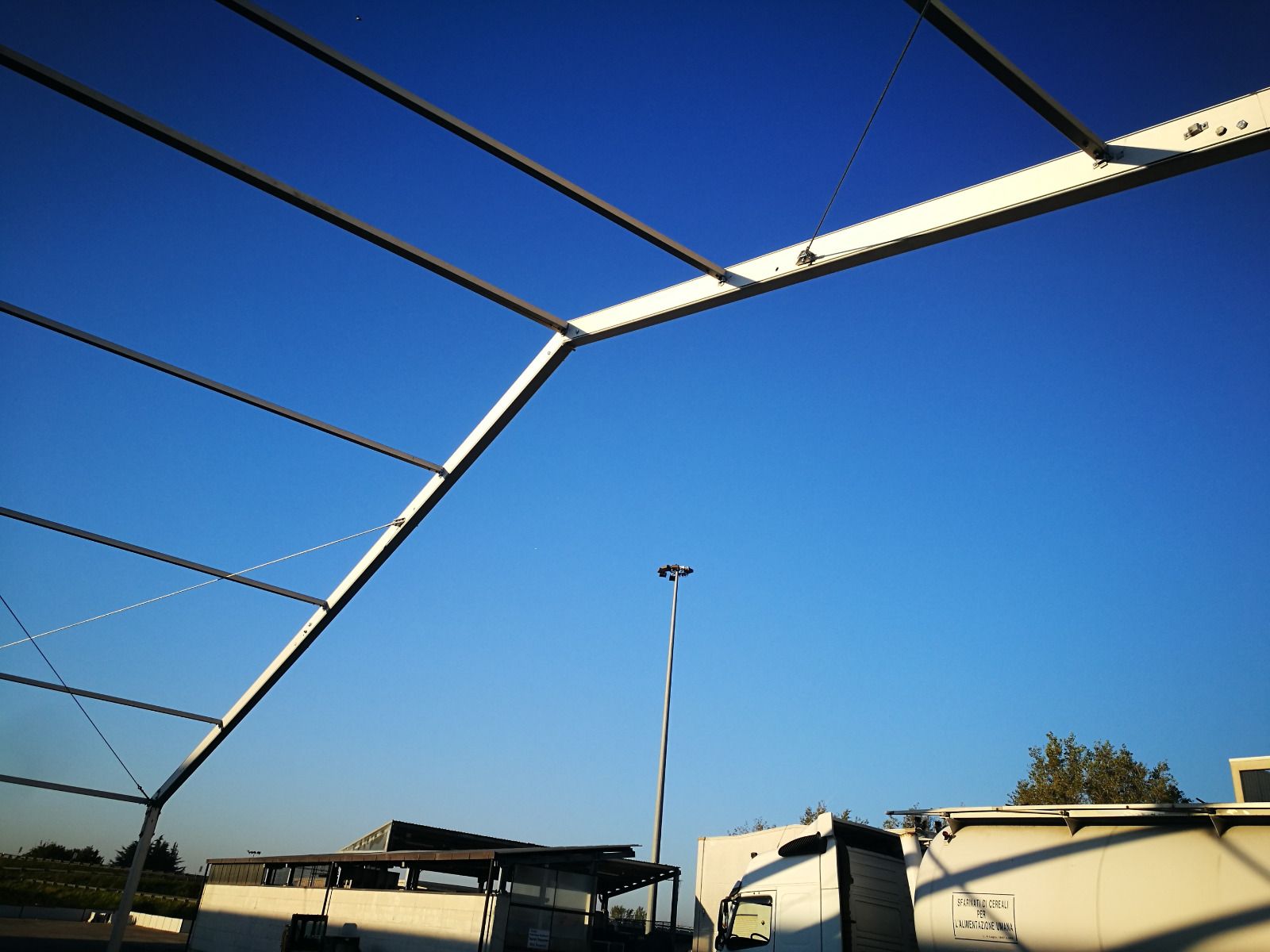 Struttura in acciaio contro un cielo azzurro brillante, con un camion e degli edifici in basso.